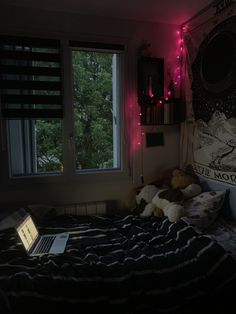 a bed room with a laptop on top of it next to a window and a wall hanging