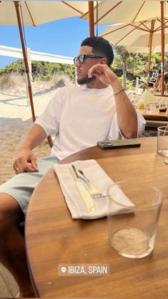 a man sitting at a table talking on a cell phone while holding a drink in his hand