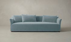 a light blue couch with four pillows on it's back and two arms, in front of a gray wall