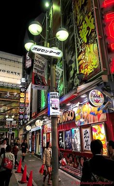 many people are walking down the street in front of some stores at night time with neon lights