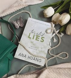 the book lies next to some flowers and a green purse on a bed with white tulips