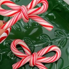 two candy canes on top of a green plate with water in the background and one being held by a woman's hand