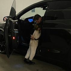 a man standing next to a black car with its door open and his hand on the door handle