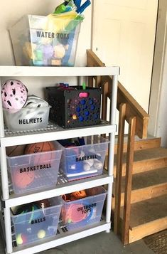 a white shelf filled with plastic containers and baskets on top of stairs next to a door