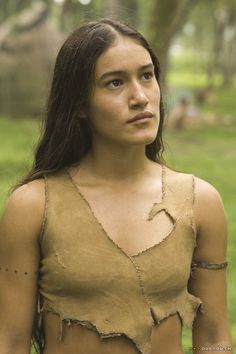 a woman with long hair wearing a brown top in the grass and looking off into the distance