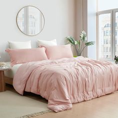 a bed with pink comforter and pillows in a room next to a large window