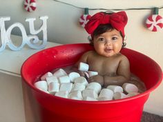 a baby sitting in a tub filled with marshmallows and wearing a red bow