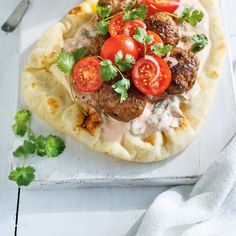 a pizza topped with meatballs, tomatoes and cilantro