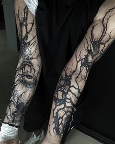 a man's arm covered in black ink with an eye and tree branches on it