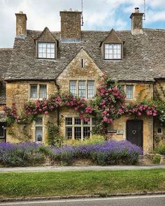 an old stone house with flowers growing on it's roof and windows in the front