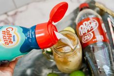 a hand holding a bottle of soda next to some limes and other drinks on a tray