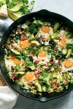 a skillet filled with eggs, avocado and other vegetables on top of a table