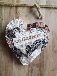 an altered heart hanging on a wooden wall with the word courageous written in red and white