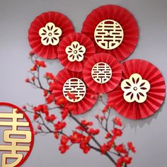 red and gold paper decorations are hanging on the wall next to a branch with flowers