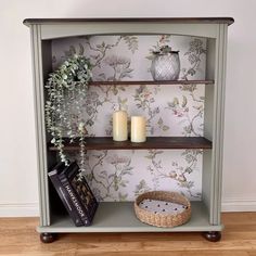 a shelf with candles and some books on it in front of a wallpapered wall