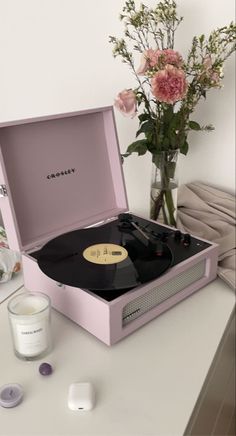 a pink record player sitting on top of a table next to a vase with flowers