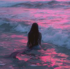 a woman standing in the ocean at sunset