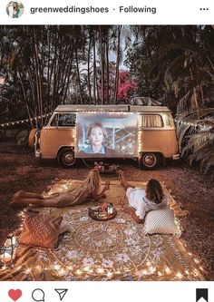 two people sitting on a blanket in front of a vw van with a screen