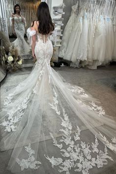 a woman standing in front of a mirror wearing a wedding dress with flowers on it