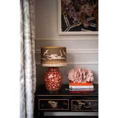 a table with a lamp, vase and books on it