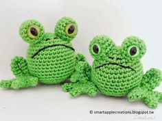 two crocheted green frogs sitting next to each other on a white surface with eyes wide open