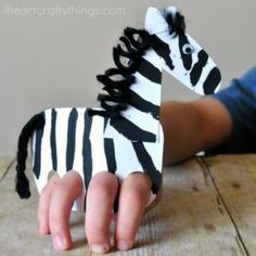 a child's hand is holding a zebra made out of paper on a wooden table