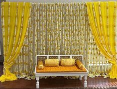 a white bench sitting in front of a yellow curtained wall with pillows on it