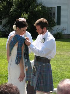 a man and woman in kilts standing next to each other on the grass with people watching