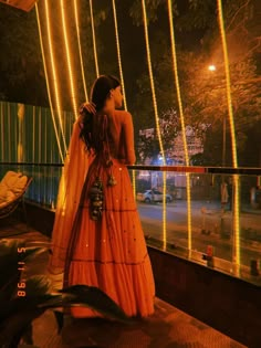 a woman in an orange dress standing on a balcony at night with lights behind her