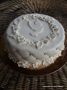 a white cake decorated with pearls and a dove on top is sitting on a wicker table