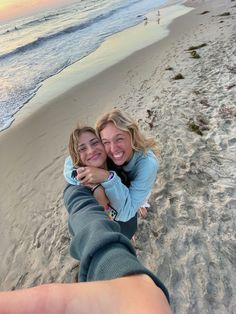 two women hugging each other on the beach at sunset with waves coming in from the ocean