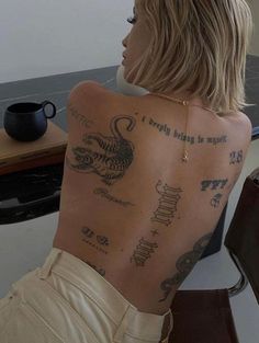 a woman with tattoos on her back sitting in front of a black table and coffee cup