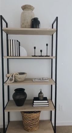 a shelf with books, vases and other items on it next to a white wall