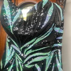 a black and green dress with silver sequins on the back, in front of a mirror