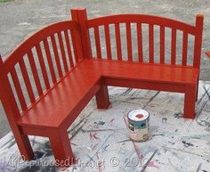 a red wooden bench sitting on top of a cement floor next to a can of paint