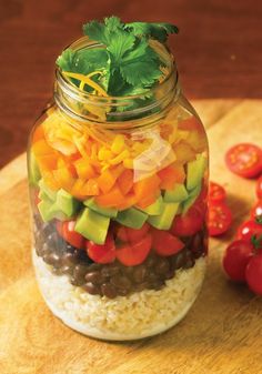 a glass jar filled with lots of different types of food on top of a wooden cutting board