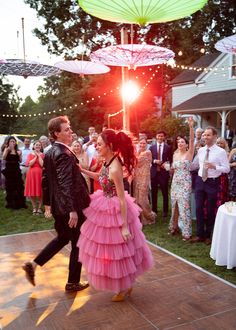 a man and woman dancing on a dance floor with umbrellas in the background at a wedding