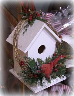 a white birdhouse decorated with evergreen and red berries