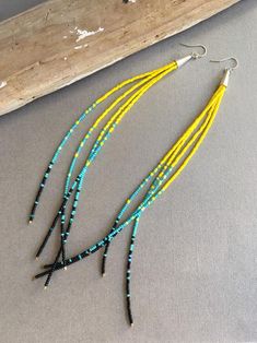 two pairs of beaded earrings with yellow and blue beads are hanging from a piece of wood