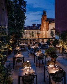 an image of a restaurant with tables and chairs in the foreground, lit up at night