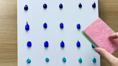 a hand is holding a sponge over a board with blue drops on it