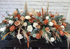 an arrangement of flowers and foliage on a black box with brick wall in the background