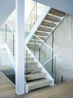 a stair case with glass railings and wooden steps in front of a white wall