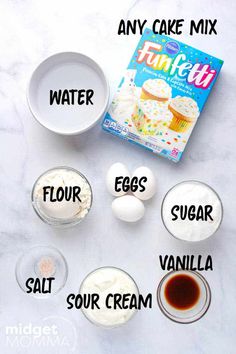 the ingredients to make cupcakes are displayed on a marble counter top, including eggs, sugar, vanilla and flour