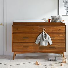 a baby's sweater hanging on a wooden dresser in a white room with toys scattered about