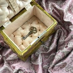 an open box with a key in it sitting on a purple cloth covered tablecloth