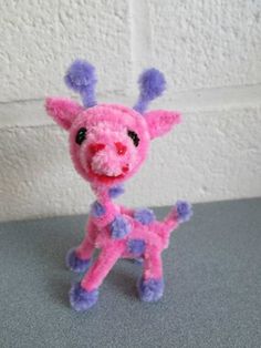 a small pink and purple stuffed animal sitting on top of a gray table next to a white wall