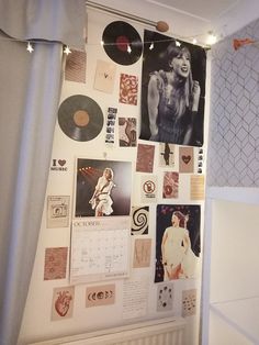 a wall covered in pictures and vinyls next to a window with curtains on it