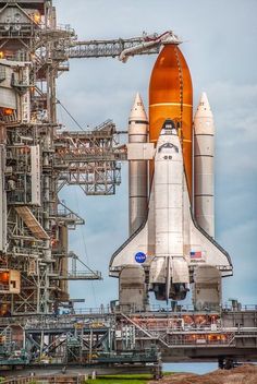 the space shuttle is on display in front of an industrial building with pipes and ladders