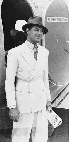 a man in a suit and hat standing next to an airplane